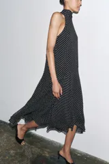 Vestido midi negro con estampado de lunares blancos, cuello halter con pañuelo integrado, sin mangas y bajo asimétrico.