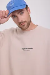 Buzo color crema de manga larga y cuello redondo, con logo 'Originals Studio Brought to you by Jack&Jones Designed in Copenhagen' estampado en el pecho.