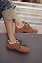 Zapatillas urbanas de cuero color tostado, con cordones verdes y suela de goma.