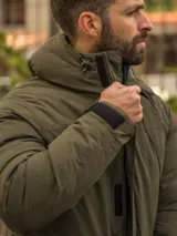 Campera verde militar con capucha, cierre frontal con cremallera y broches, bolsillos laterales con solapa y puños ajustables con velcro.