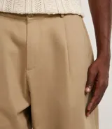 Pantalón masculino estilo sastre, corte balloon (holgado con volumen y talle alto), color beige. Presenta pliegues frontales y cierre tradicional.