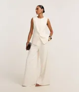 Pantalón pantalona de corte sastre color crudo, confeccionado en tejido plano de poliéster. Tiene trabillas en la cintura, cierre tradicional, elástico y lazo en la cintura, pliegues delanteros y bolsillos falsos traseros.