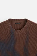 Sweater marrón de punto con cuello redondo y manga larga. Tiene un estampado irregular con efecto spray en color azul.