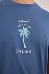 Remera azul de algodón con cuello redondo y estampado de una palmera con texto en el frente.