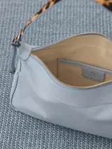 Cartera tipo baguette color celeste, confeccionada en cuero vacuno flor. Incluye correa regulable en combinación de cuero y pelo vacuno, con hebillas metálicas personalizadas.