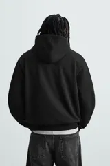 Sudadera con capucha color crudo, de corte relajado, confeccionada en tejido de algodón con interior rizado. Cuenta con cuello con capucha, manga larga, bolsillo frontal tipo canguro y acabados en rib.