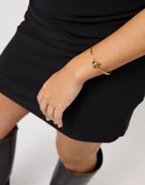 Pulsera rígida dorada con cierre frontal en forma de estribo y un pequeño topacio blanco engarzado.