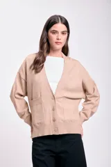 Cardigan de punto color beige con corte lateral, escote en V, cierre con botones y bolsillos frontales.