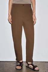 Pantalón marrón de tiro medio con trabillas en la cintura, bolsillos laterales, pinzas delanteras y bajo ajustable con trabilla y botón.