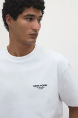 Remera blanca de corte holgado con cuello redondo y estampado pequeño con la frase "New York" en el pecho.