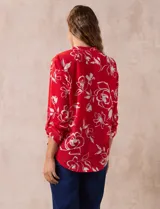 Blusa de gasa roja con estampado floral blanco, cuello a la base con escote en V y mangas 3/4 regulables con presilla y botón.