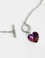 Collar corto dorado con cadena de eslabones retorcidos y dije de corazón de cristal color lila.