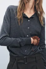 Chaqueta de punto fino color gris oscuro confeccionada con lana. Tiene cuello redondo, manga larga y cierre frontal con botones.
