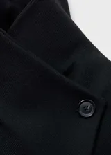 Abrigo largo negro con cuello de solapa, cierre cruzado con lazo, bolsillos laterales y trabillas.
