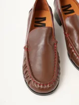 Mocasines de cuero color marrón con apliques de charol y pespuntes rojos.