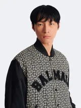 Campera Balmain estilo varsity con estampado monogrammed en blanco y negro, mangas largas negras y cierre frontal con botones a presión.