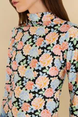 Top de cuello alto y mangas largas con estampado floral multicolor sobre fondo negro.