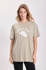 Remera color arena de corte oversize con estampa de un sombrero de cowboy y la frase "Wild & Free" en blanco.