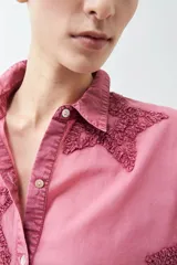 Camisa fucsia de manga larga con cuello camisero y cierre frontal con botones. Presenta apliques de estrellas bordadas en el frente y en el cuello.