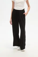 Pantalón deportivo negro de corte holgado, con cintura elástica, bolsillos laterales y botones a presión en las costuras laterales de las piernas.