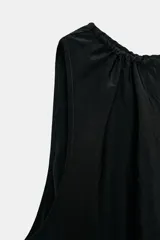 Vestido midi negro, sin mangas, con cuello redondo y frunces en el escote. La falda tiene un corte asimétrico con terminación en punta en el bajo.