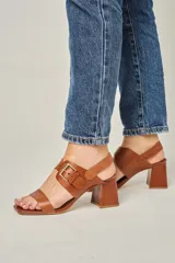 Sandalias de cuero color champagne, con punta cuadrada, tira ancha sobre el empeine y tira al tobillo con hebilla metálica. Taco cuadrado de 7 cm.