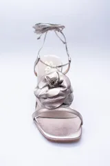 Sandalias de cuero color champagne, con taco cuadrado, tira delgada sobre los dedos y tobilleras para atar. Presentan un aplique de flor de cuero en la capellada.