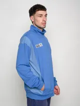 Buzo azul de felpa con medio cierre, cuello alto y mangas largas. Presenta el escudo del Club Nacional de Football en el pecho y el logo de Umbro en la manga.