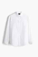 Camisa blanca de manga larga con cuello inglés, tapeta lisa, canesú en la espalda y bajo redondeado. Corte estándar para una silueta clásica y cómoda.