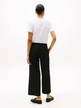 Pantalón negro de corte amplio, tobillero y talle bajo. Confeccionado en tejido antiarrugas de mezcla de viscosa elástica. Presenta cierre de cremallera con enganche oculto, raya marcada en la parte delantera y trasera, y dos bolsillos traseros de ojal.