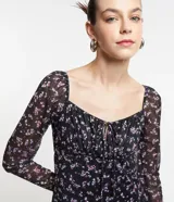 Vestido midi de tul negro con estampado floral liberty en tonos lila, escote cuadrado con lazo, mangas largas y abertura lateral.