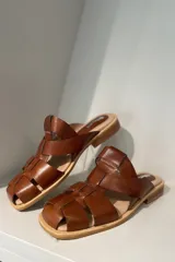 Zueco marrón de cuero vacuno con diseño de tiras entrecruzadas y suela plana.