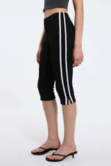 Calzas capri negras con cintura elástica y una raya blanca vertical a lo largo de la pierna.