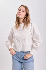 Blusa color crudo con cuello redondo, mangas largas abullonadas y detalle de plisado y encaje en el frente.