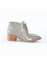 Botines grises de cuero charol brillante, con cordones frontales y tacón bloque de madera clara.