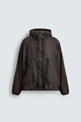Cazadora de tejido técnico ripstop color marrón oscuro, con cuello alto y capucha ajustable, mangas largas con puños elásticos, bolsillos frontales con cremallera oculta, bajo ajustable con elástico lateral y cierre frontal con cremallera.