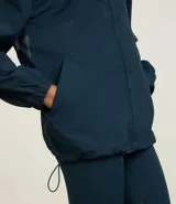 Campera deportiva tipo cortavientos en color azul petróleo, con cuello alto y cierre frontal completo. Presenta recortes de tul translúcido en los laterales, puños elásticos y bolsillos funcionales. Confeccionada en tejido de poliamida.