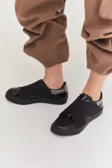Zapatillas con diseño de bandas cruzadas en tonos negro y marrón, con suela blanca.
