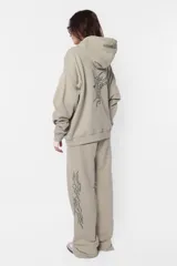 Buzo hoodie de frisa color beige, de silueta oversize, con puños y cintura de rib al tono, capucha forrada en su interior, bolsillo canguro, cordones con ojalillos y punteras metálicas personalizadas con marca, tanca para regular cordones, remaches en boca de bolsillo y bordado en espalda a contratono.