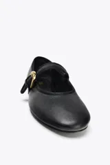 Zapato plano tipo bailarina color negro, confeccionado en piel, con tira sobre el empeine y hebilla metálica dorada ajustable. Tiene punta redonda y suela de 1.5 cm de altura.