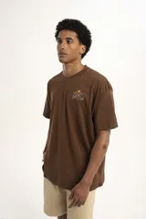 Remera marrón con cuello redondo, corte holgado y estampado pequeño de flores y texto en el pecho.