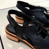 Zapato tipo sueco de cuero vacuno negro con textura reptil, con cordones y talón descubierto. Tiene suela de madera con altura de 4,5 cm en el talón y 1,5 cm en la parte delantera.