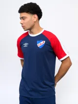 Remera de algodón azul con mangas raglán rojas y detalles blancos en cuello y puños. Incluye logo de Umbro bordado en el pecho y escudo del Club Nacional de Football.