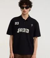 Remera boxy de mangas cortas, confeccionada en algodón, color negro, con cuello polo y lettering "93 MAD" y una cruz estampada en la parte delantera.