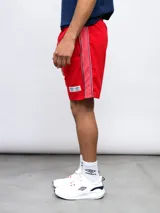 Bermuda deportiva azul marino con cordón ajustable en la cintura y bolsillos laterales. Presenta el escudo del Club Nacional de Football bordado en la pierna izquierda y un logo de Umbro en la pierna derecha. Tiene una franja blanca y roja en los laterales.