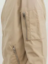 Campera bomber color beige con cuello de béisbol, cierre con cremallera, bolsillos frontales con cremallera y bolsillo en la manga.