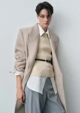 Chaleco de punto color crema, con cuello redondo y diseño sin mangas. Ajustado al cuerpo y con cinturón fino de cuero marrón.