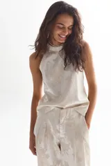 Top sin mangas color crema con estampado floral dorado, cuello halter y cierre con botón en la nuca.