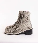 Bota corta de cuero charol negro, con caña baja, cierre lateral y taco cuadrado de madera.