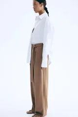 Pantalón sastrero marrón de punto con tiro alto, elástico oculto en la cintura, cierre decorativo, cinturón cosido con anillas en D de metal en un lateral y piernas ajustadas con pinzas para estilizar la silueta.